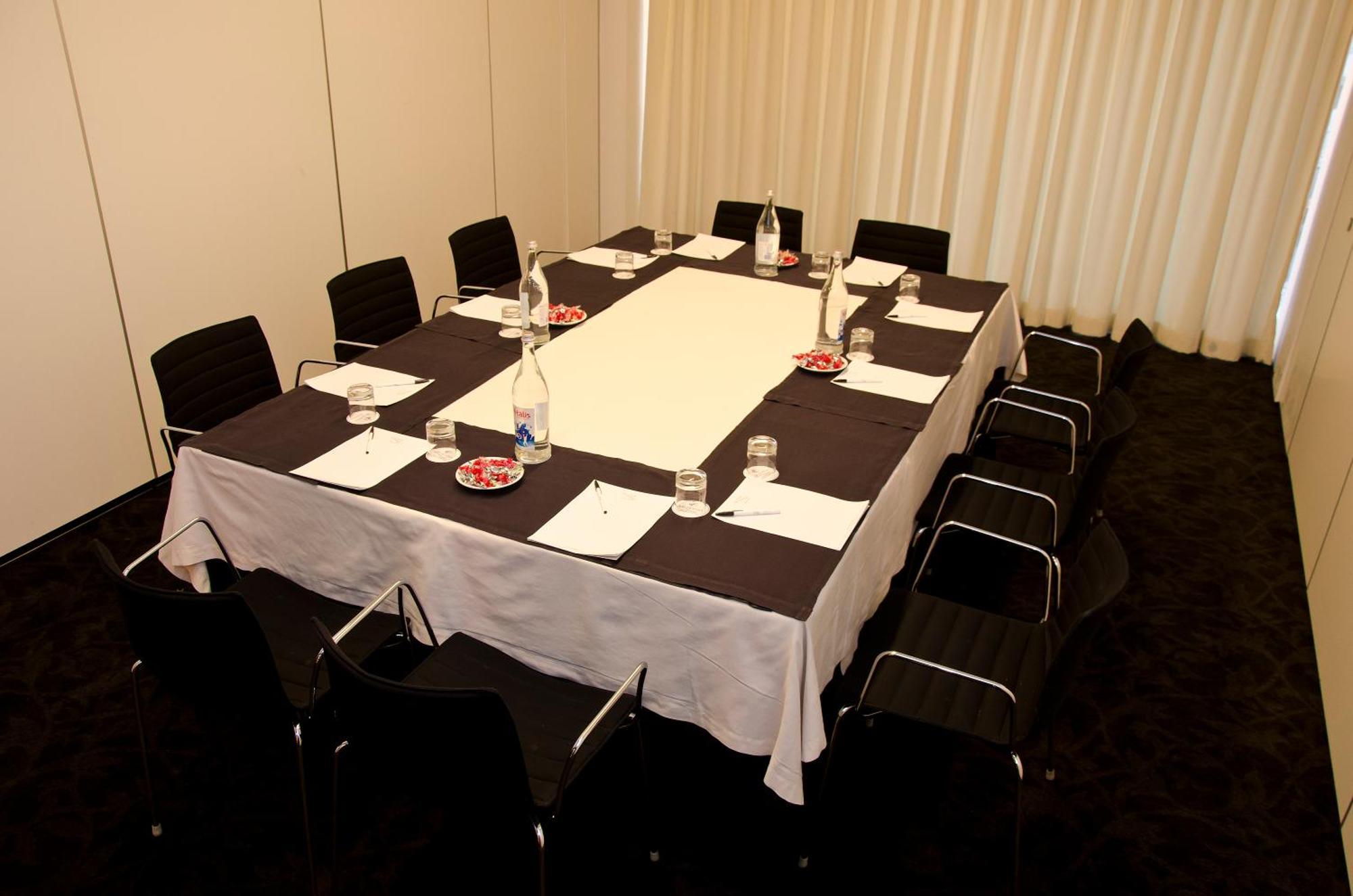 Vip Grand Lisboa Hotel & Spa Exterior photo The image shows a conference or meeting room setup. In the center, there is a rectangular table covered with white and black tablecloths. Surrounding the table are several black chairs. On the table, there are plates, glasses of water, and papers, li