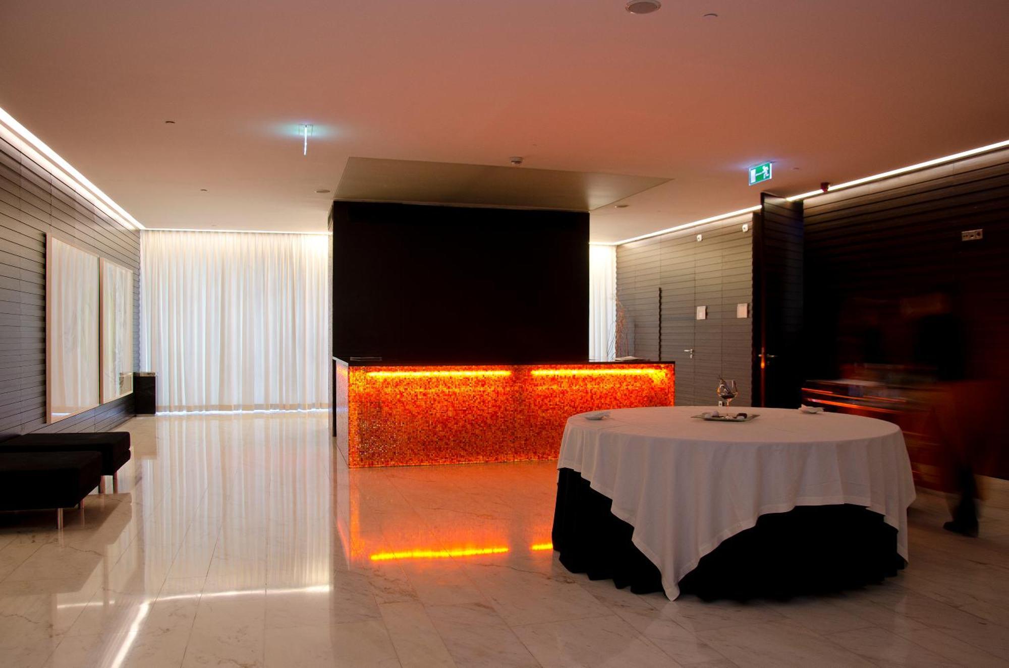 Vip Grand Lisboa Hotel & Spa Exterior photo The photo depicts a modern interior space, possibly a lobby or reception area. It features a sleek, minimalist design with a polished marble floor. There is a large table covered with a white tablecloth in the foreground, and a stylish reception desk