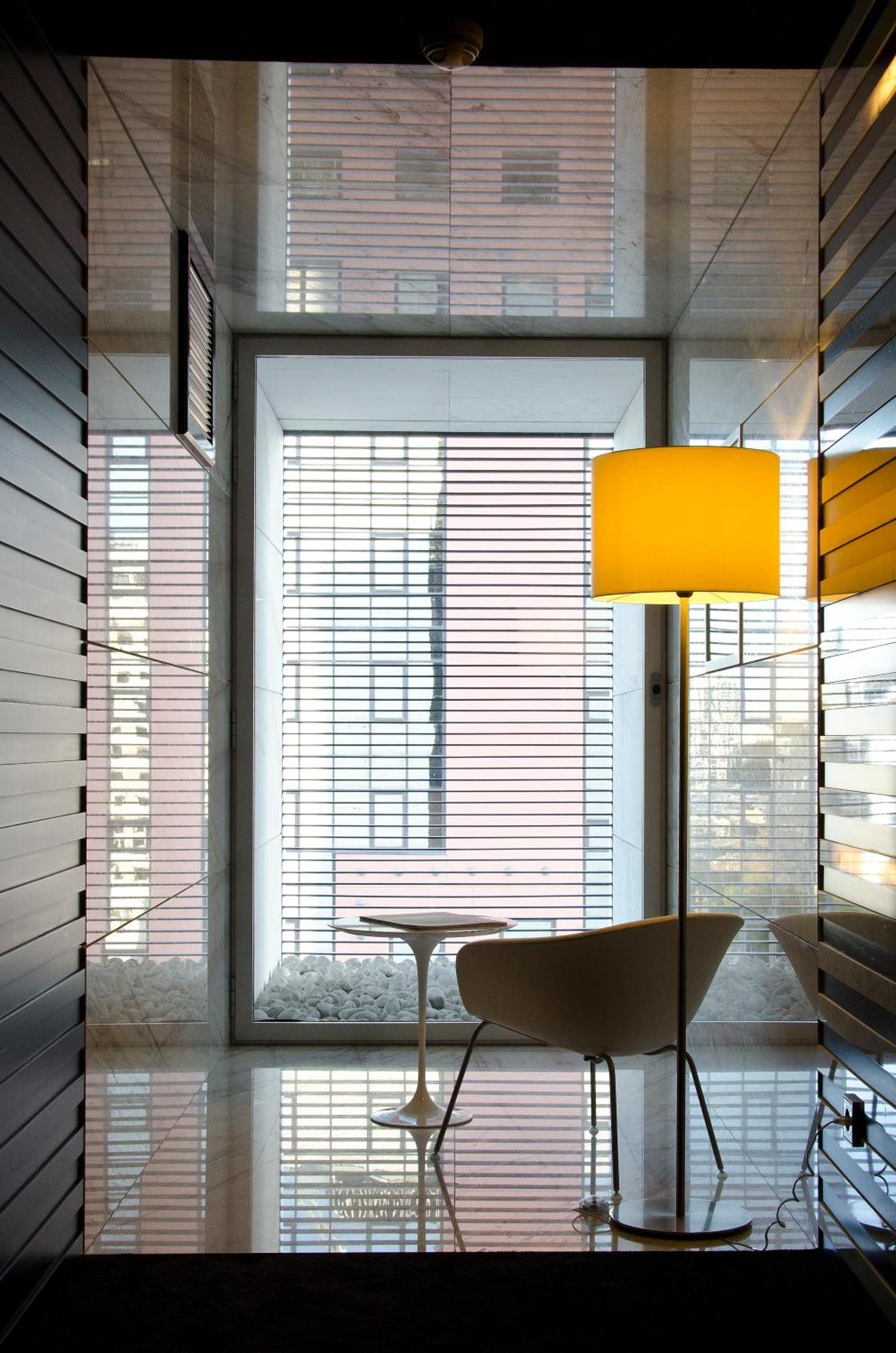 Vip Grand Lisboa Hotel & Spa Exterior photo The photo shows a modern interior space with a large window featuring horizontal blinds. A warm yellow lamp stands beside a small table, creating a cozy atmosphere. The walls appear to be sleek and minimalistic, possibly made of light-colored materia