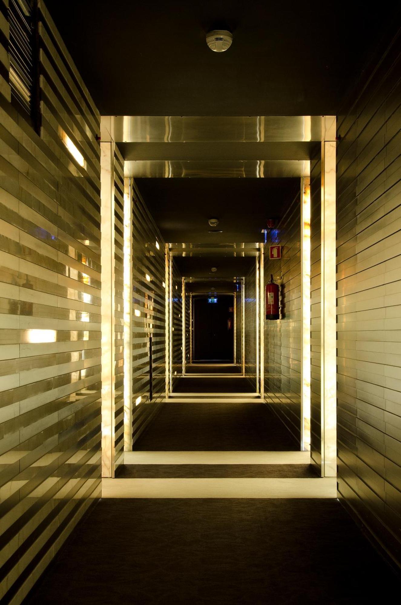 Vip Grand Lisboa Hotel & Spa Exterior photo The photo shows a long, narrow hallway with a modern design. The walls are lined with reflective panels that create a shimmering effect. The corridor is illuminated with a series of lights, emphasizing the geometric lines and depth of the hallway. At