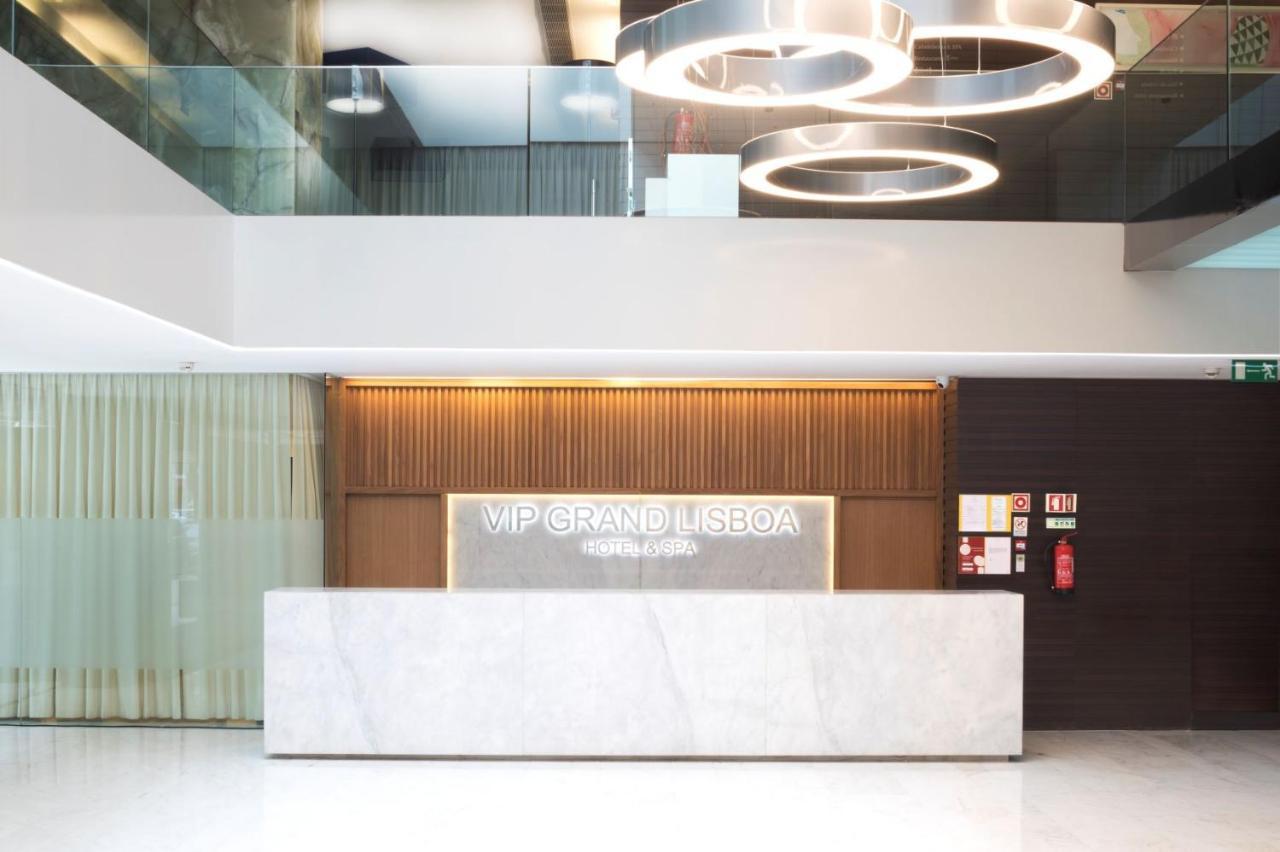 Vip Grand Lisboa Hotel & Spa Exterior photo The photo shows the interior of a hotel lobby, specifically the reception area of the "VIP Grand Lisboa." The reception desk is modern and minimalist, made of marble, with an illuminated sign displaying the hotel name. Above the reception area, there